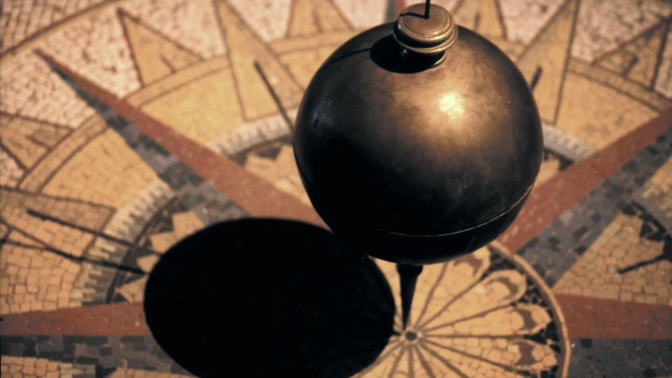 A heavy pendulum bob swinging over a compass-rose floor