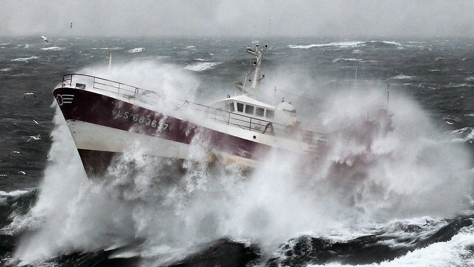 A fishing boat crashing through large waves in a storm